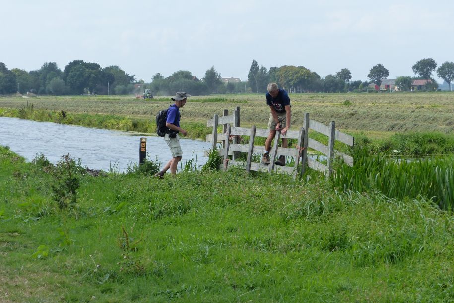 Twee wandelaars klimmen over een hek tijdens een tocht door het westen van Nederland.